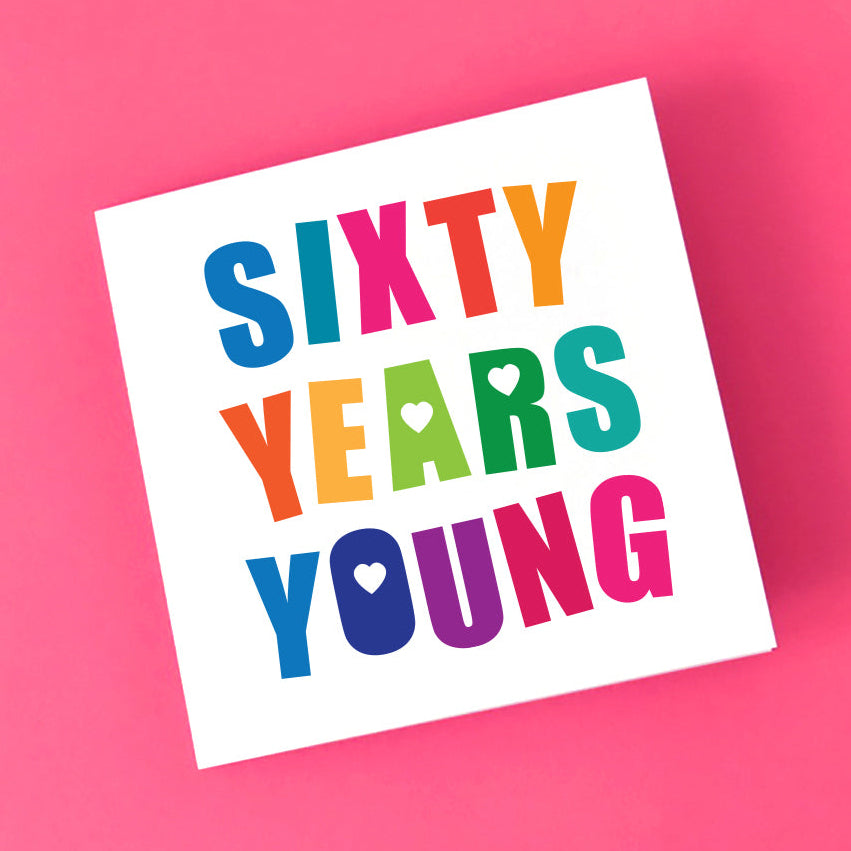 Angled view of a vibrant "Sixty Years Young" card, highlighting the bold, bright, multi-coloured letters and the cute love heart details. Perfect for a milestone 60th birthday.