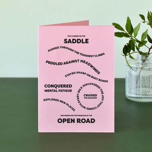 Pink A6 card with bold black text that reads "You climbed on the saddle, pushed through the toughest climbs, peddled against headwinds, stayed sharp on busy roads, conquered mental fatigue, discovered the joy that comes with every mile, cruised the descent, explored new places and embraced the freedom of the open road."