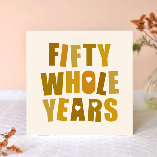 Cream square card with the words Fifty Whole Years in big bold font in shades of gold. Some of the letters are punched with love hearts.