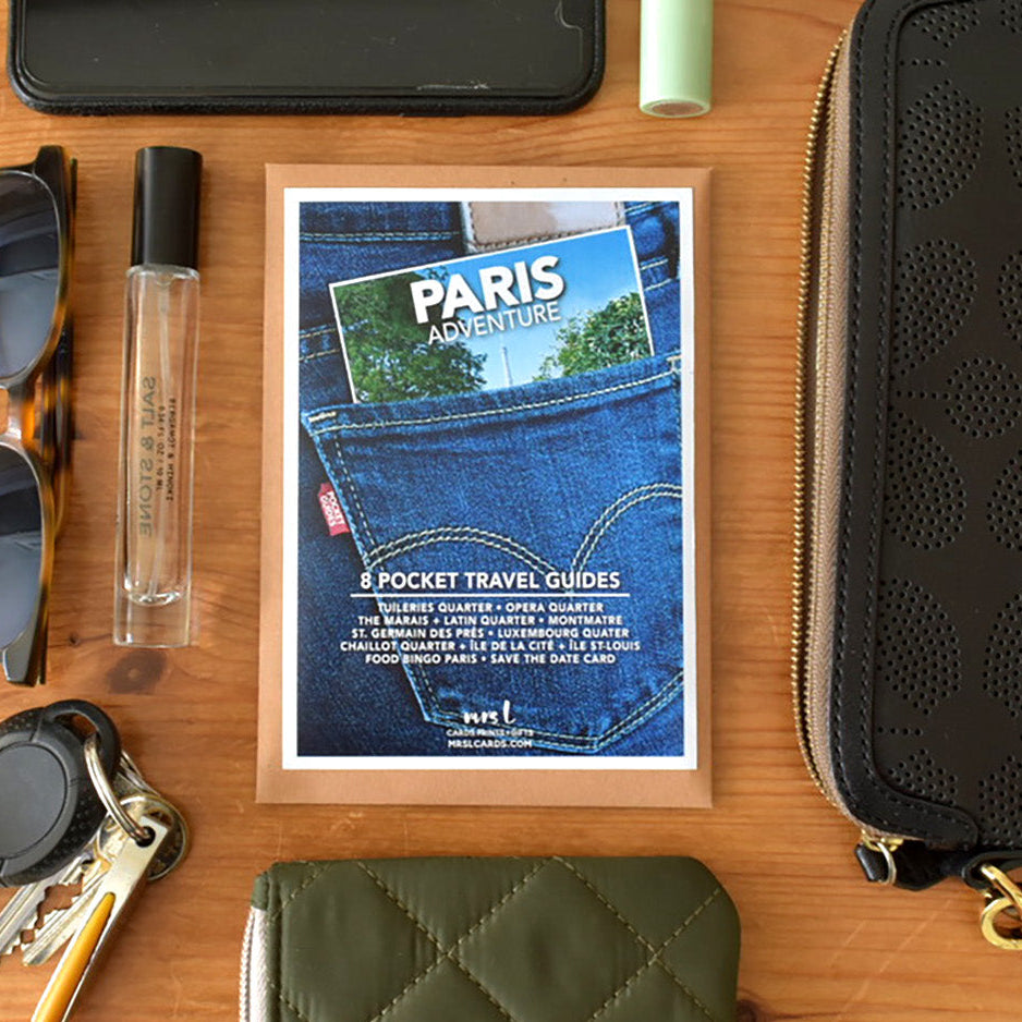 Collection of travel items including sunglasses, perfume, the Paris Pocket Guide, a wallet - all to fit inside a small black handbag.