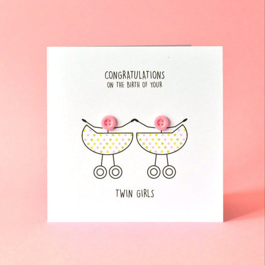 Square white card featuring a simple line drawing of two prams with little girls inside. The heads of the little girls are made from pink buttons stuck on to the card. The wording on the card reads "Congratulations on the birth of your Twin Girls".