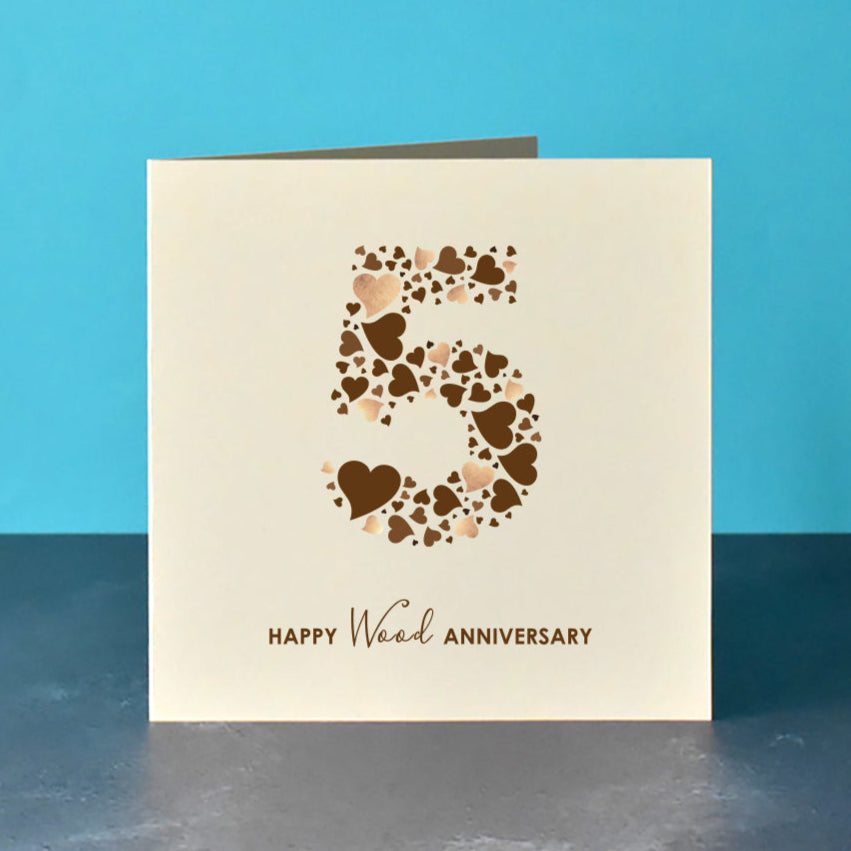 Square cream card with a large 5 in the centre. The 5 is made from a collection of brown love hearts some with a printed shimmer. Underneath the number 5 is the message "Happy Wood Anniversary".