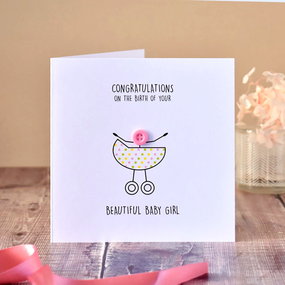 Baby girl birth congratulations card with a pram illustration and a cute stick figure baby with pink button head.