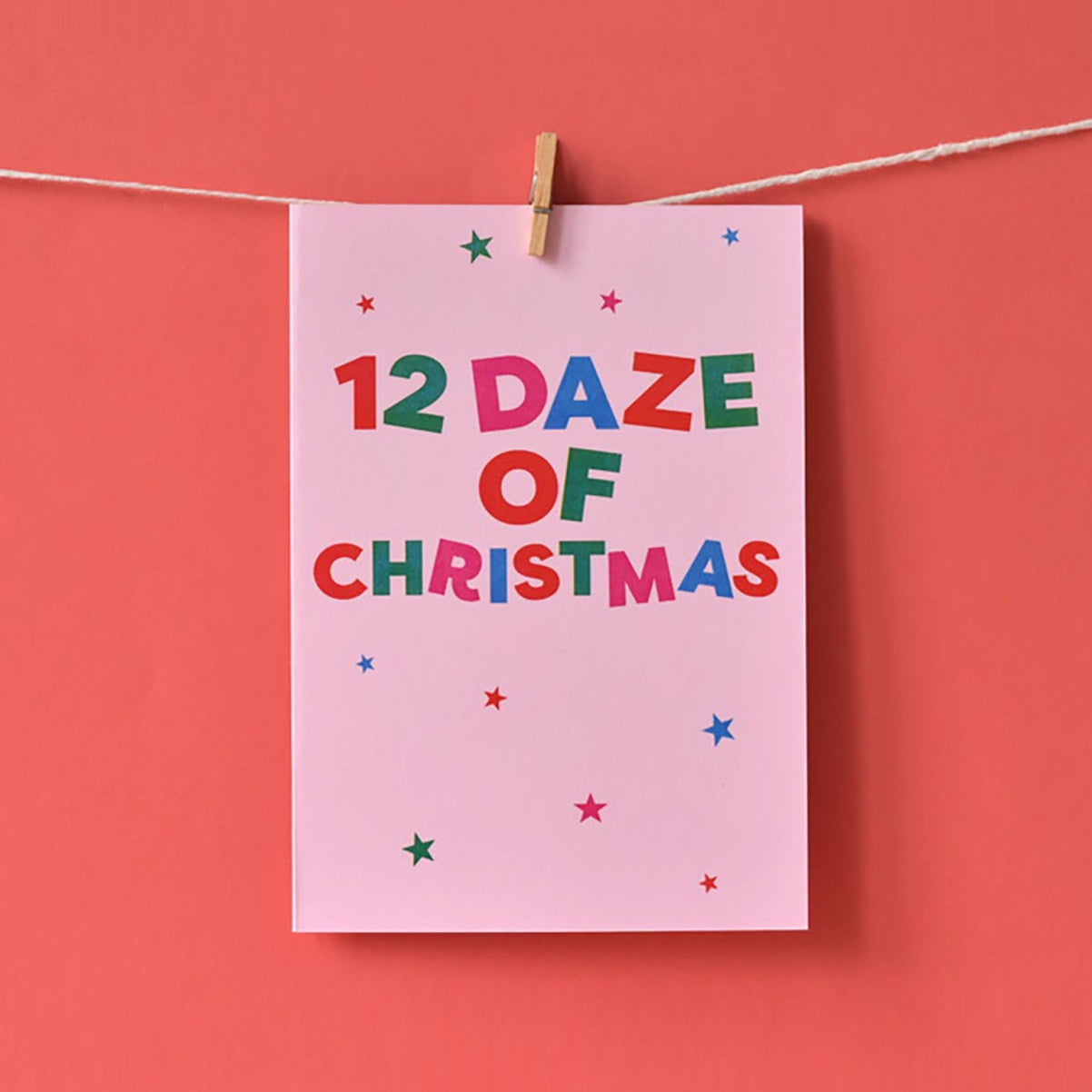 Card with '12 Daze of Christmas' text hanging on a string against a red background
