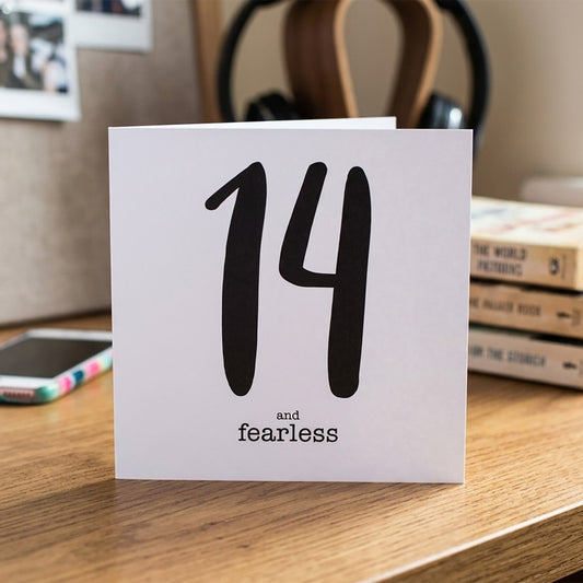 Card with '14 and fearless' text on a desk with books and a phone in the background