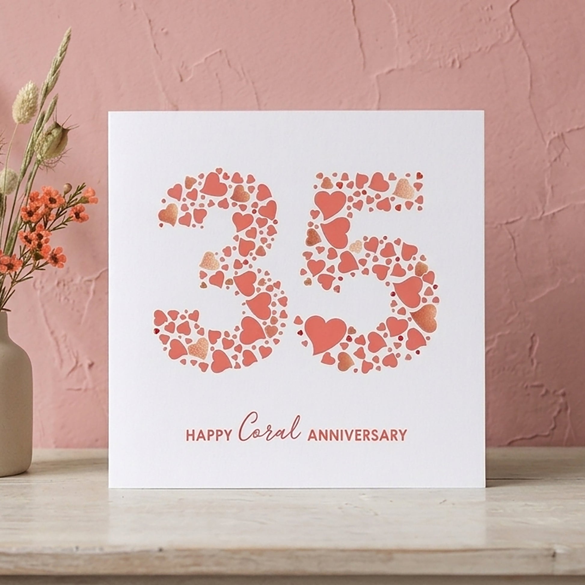 Wedding anniversary card with the number 35 made from lots of love hearts and 'Happy Coral Anniversary' text on a pink background with a vase of flowers.