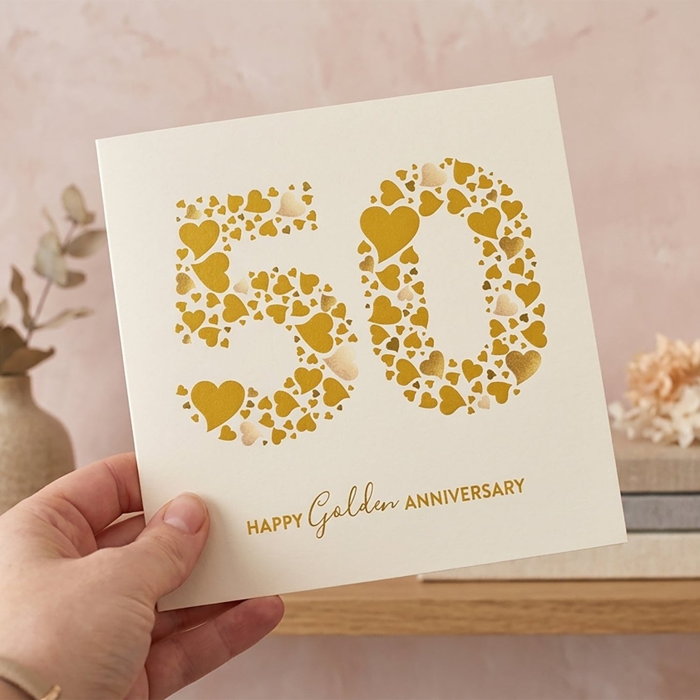 Card with '50' made of hearts and 'Happy Golden Anniversary' text held by a hand.