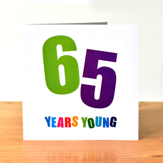 Square white birthday card with the large, bold number "65." The "6" and "5" are each angled differently and presented in unique bold colours. of green and purple Below, the words "Years Young" are written, with each letter in a distinct bold colour.