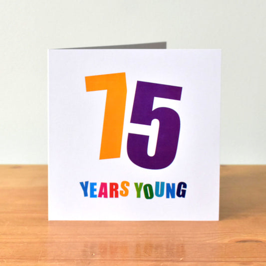 Square white birthday card displaying the large, bold number "75." Both the "7" and "5" are set at contrasting angles and in different bold colours. Underneath the number, "Years Young" is written, with each letter in a separate bold colour.