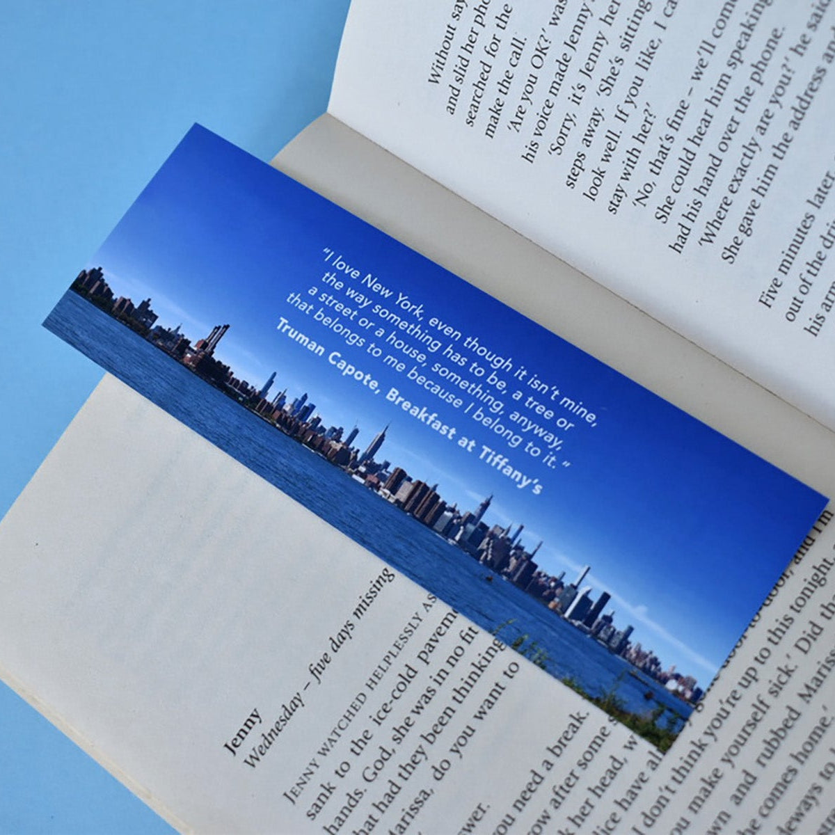 Open book with a bookmark featuring a silhouette of a city skyline, and a quote from the book Breakfast at Tiffany's.