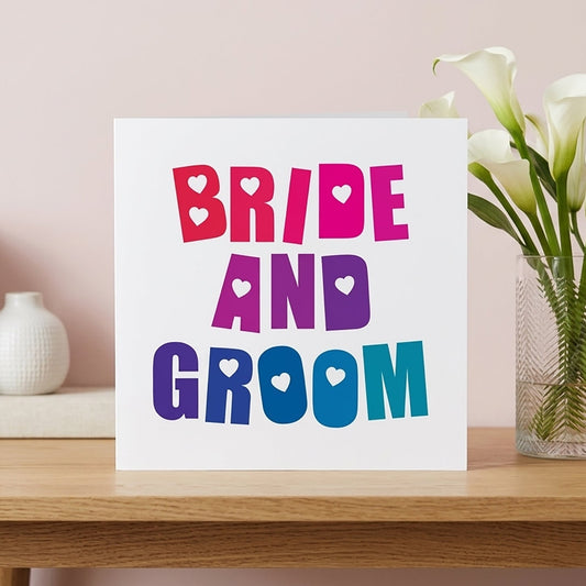 A square white bride and groom wedding card featuring bold modern typography blended from vibrant red to deep blue with hidden love hearts.