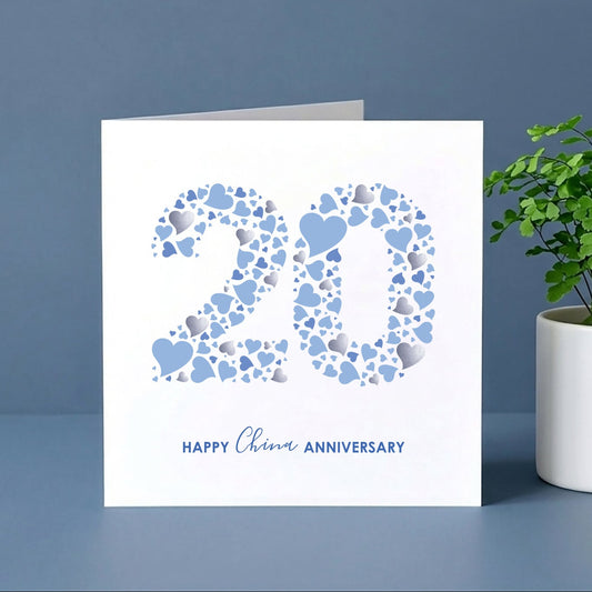 Card with '20' design and 'Happy 20th Anniversary' text next to a plant on a blue background