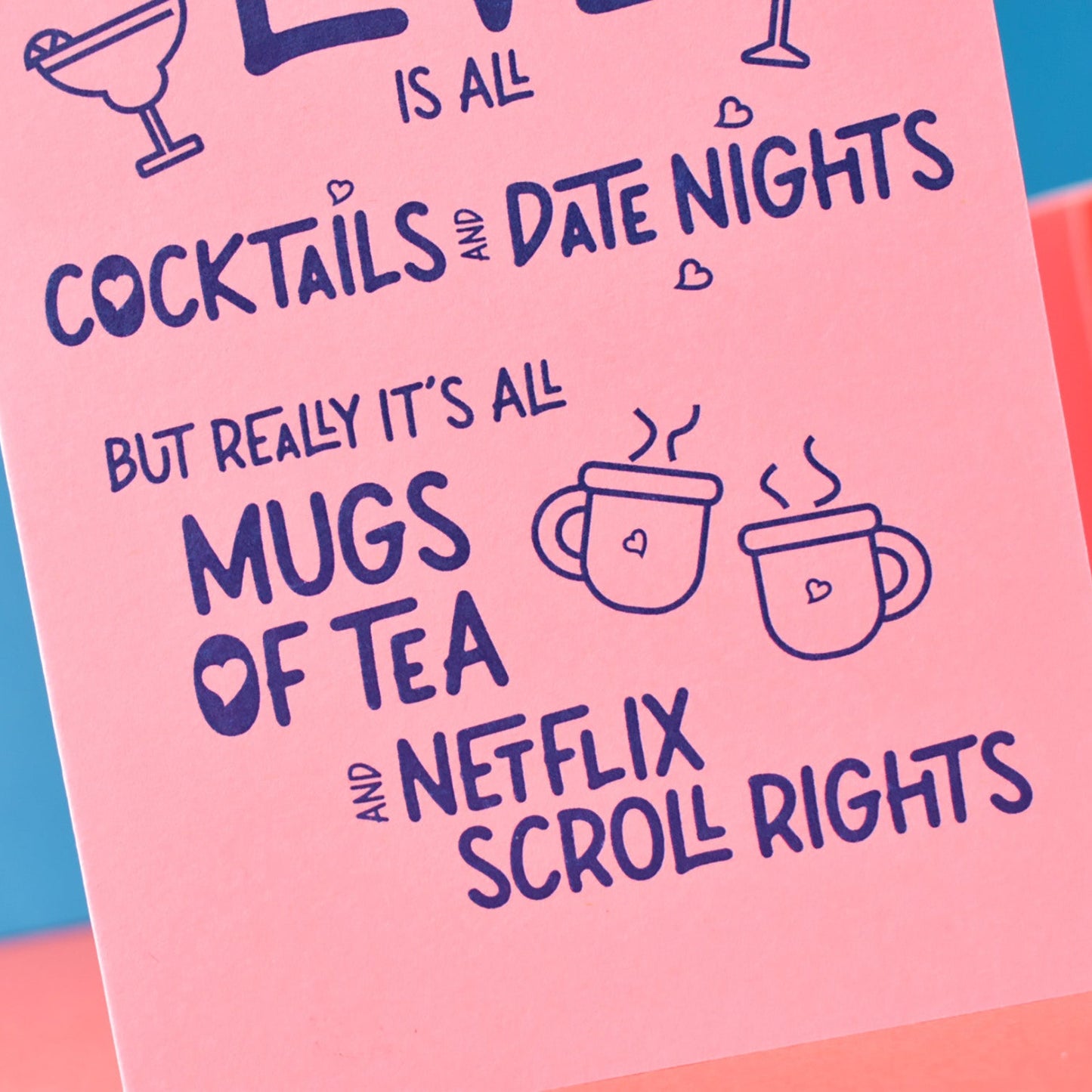 Pink card with text about tea, mugs, and Netflix, placed on a red surface with a blue background.