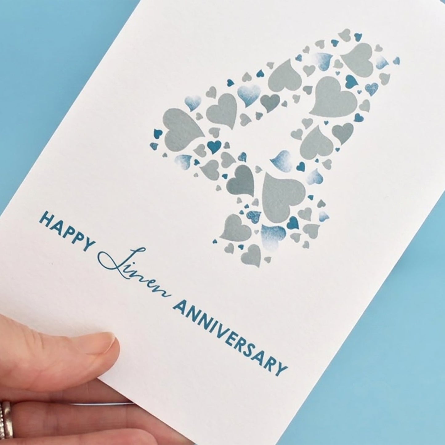 Hand holding a card with heart design and 'Happy 4th Anniversary' text.