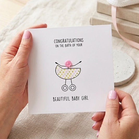 Hand finished new baby girl congratulations card featuring a classic pastel pram design with a pink button head.