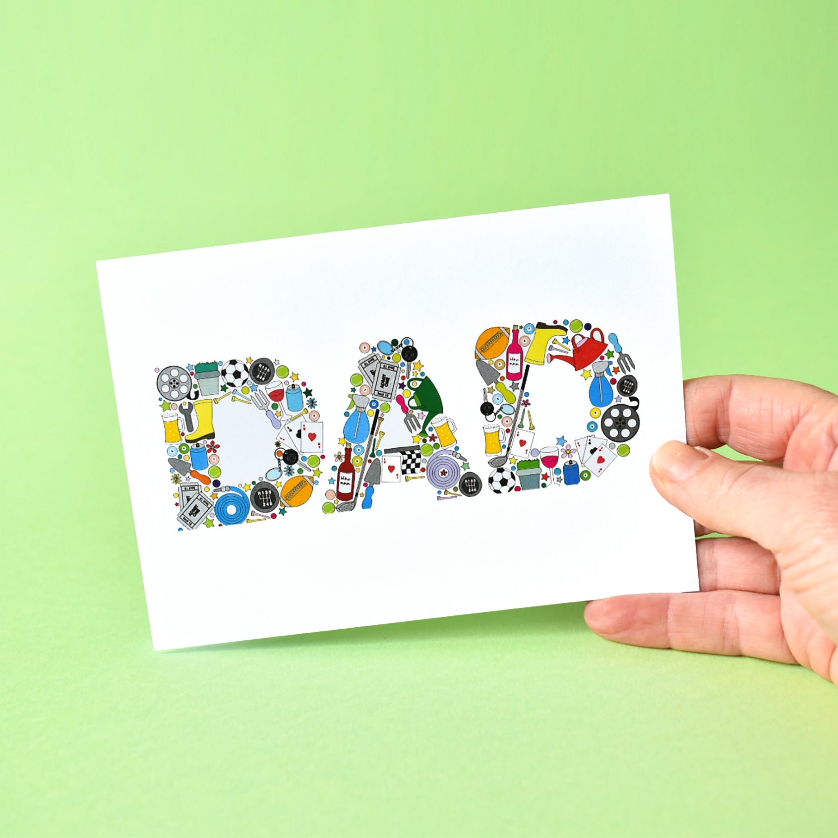 White A6 card with the word Dad written in capital letters and made from illustrations of such things as: footballs, gardening hose, trowel and watering can, pint of beer, bottle of wine, plants, film reel, playing cards, rugby ball, gold clubs and balls, cinema tickets, tennis balls and snooker balls.