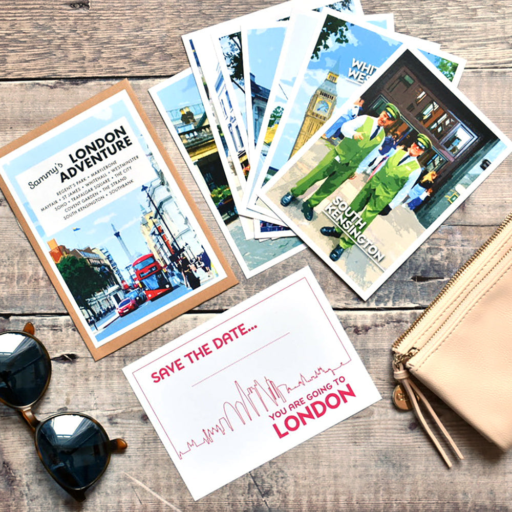 A styled flat-lay featuring a London-themed 'Sammy's London Adventure' kit, a fanned-out selection of London travel guides, a 'Save the Date' card, black sunglasses and a pink zippered pouch on a rustic wooden background.