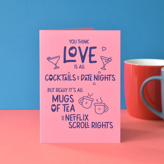 Pink card with humorous text about love and mugs of tea, against a blue and pink background with two mugs. Text reads ""You think love is all cocktails and fancy date nights, but really it's all mugs of tea and Netflix scroll rights."