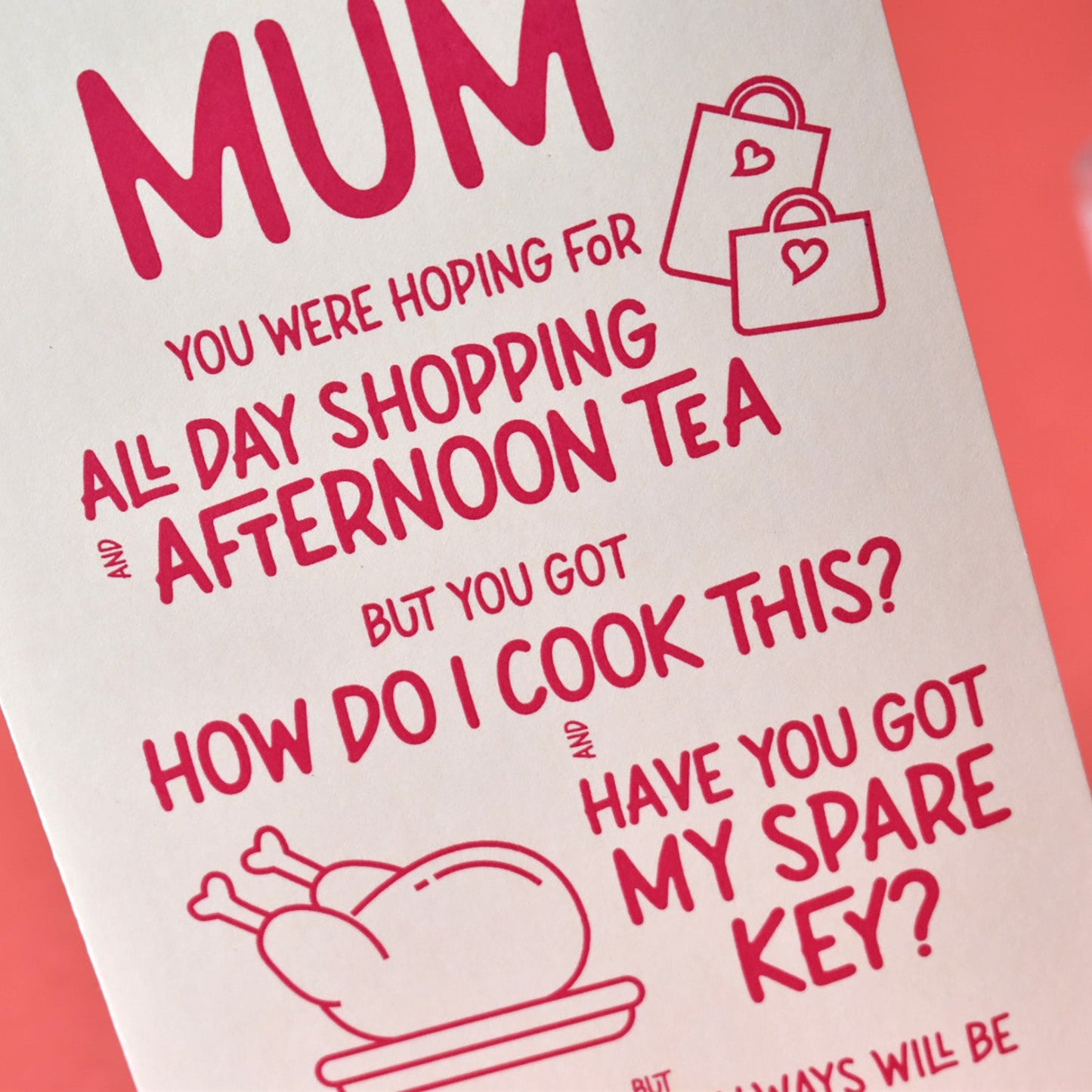 Cream Mother's Day card with pink and red text about spare keys and cooking, shown on a colourful background in soft natural light.