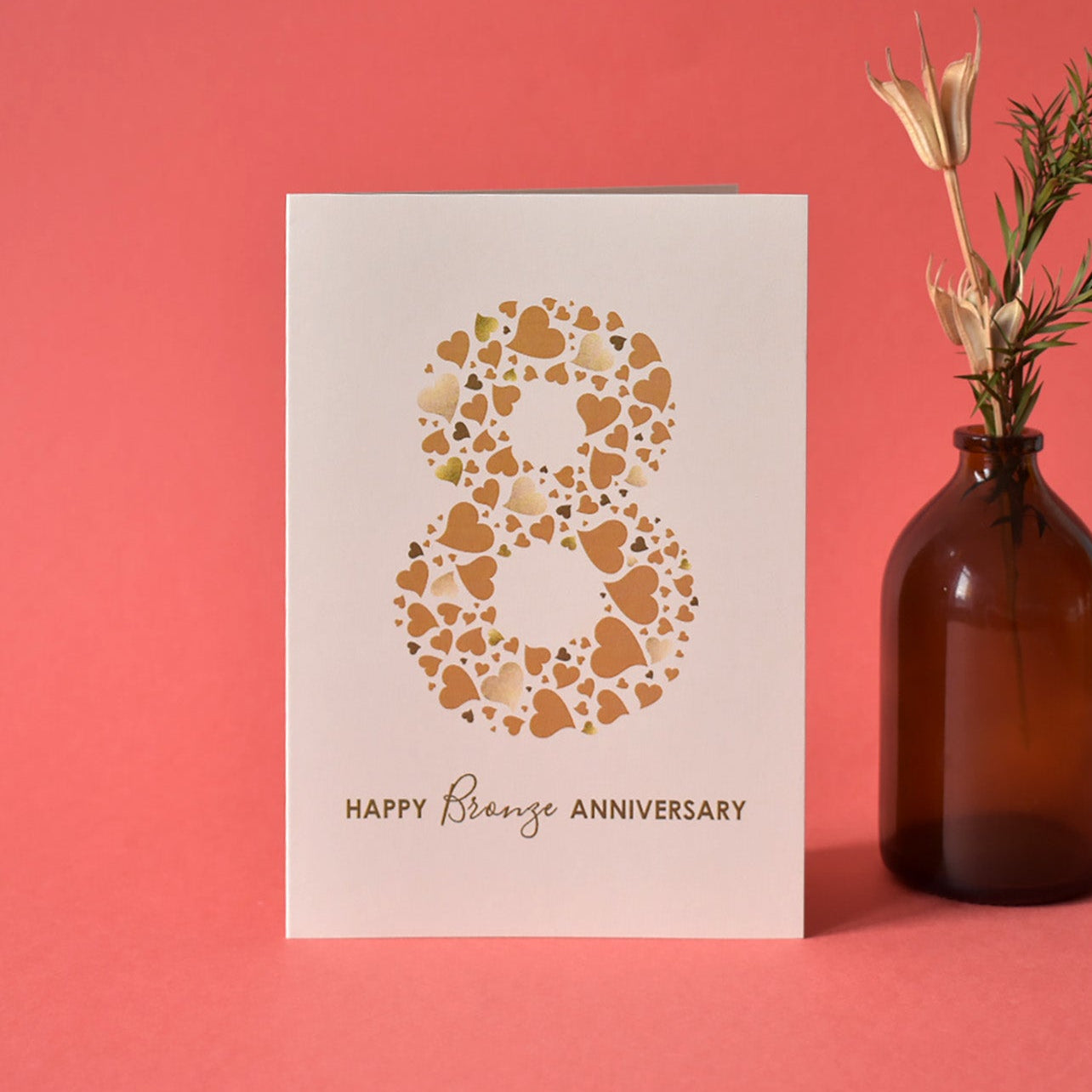 8th Wedding Anniversary Card with a large number 8 made from a collection of bronze love hearts, some with a shimmering print centre stage on a cream A6 card. Underneath the number 8 are the words Happy Bronze Anniversary.