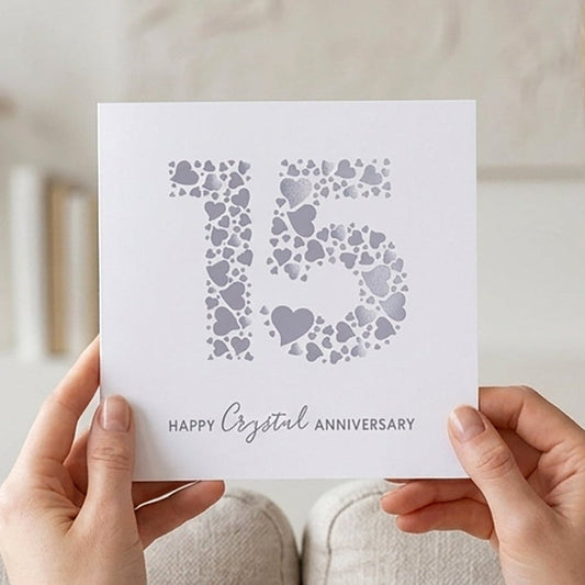 Person holding a card with '15 happy Crystal anniversary' text in a cozy living room.