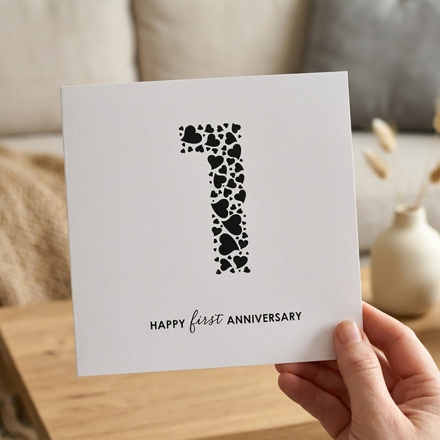 Square white card with large black number 1 made from a collection of love hearts. Underneath the words read "Happy First Anniversary".