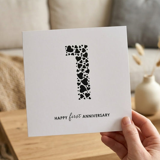 Square white card with large black number 1 made from a collection of love hearts. Underneath the words read "Happy First Anniversary".