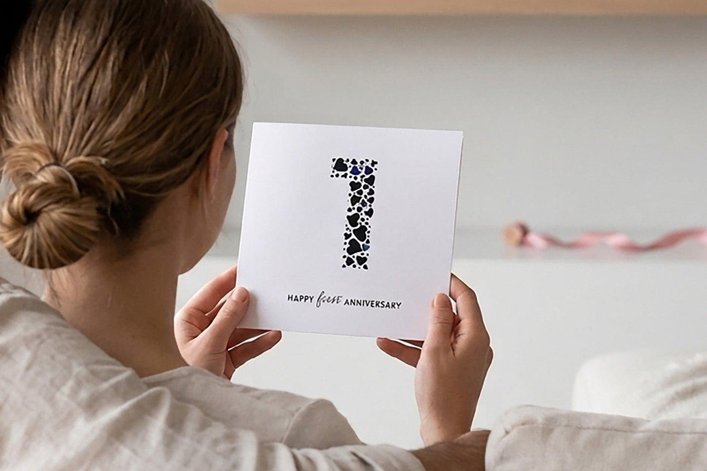 Couple sitting on a couch holding a card with text, in a cozy living room setting.