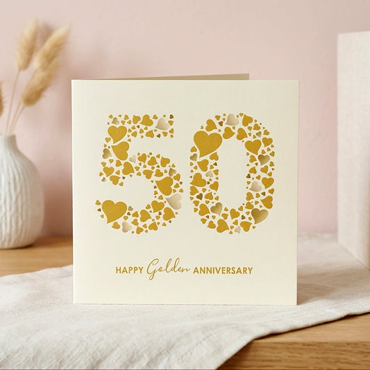 Card with '50' made of hearts and 'Happy Golden Anniversary' text on a table with books and a vase.