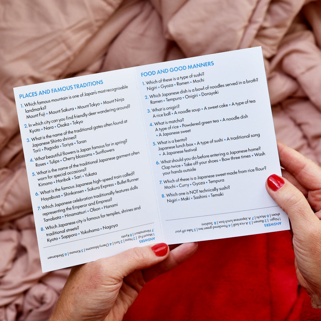 A person holding a printed trivia quiz with questions about places and food and manners, set against a soft pink textured fabric background.