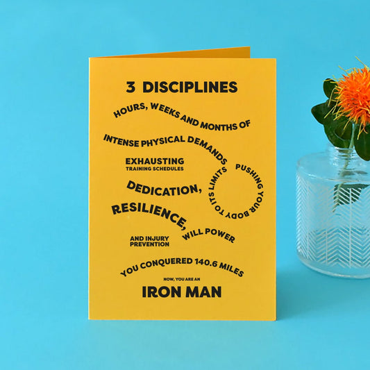 Bright yellow A6 card with bold, black text reading "3 disciplines, hours, weeks and months of intense physical demands, exhausting training schedules, pushing your body to the limits, dedication, resilience, will power and injury prevention, you conquered 140.6 miles. Now you're an Ironman."
