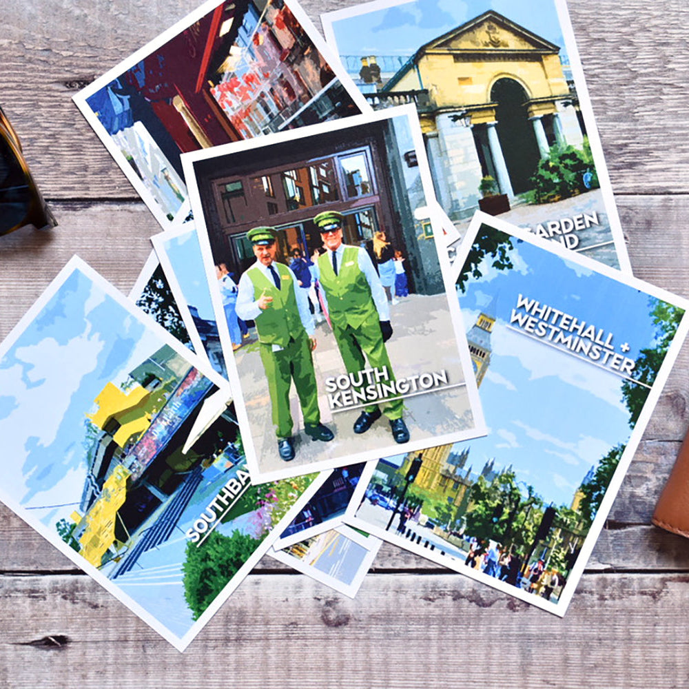 A fan of printed London Guides showing colourful landmarks and text like 'South Kensington' and 'Whitehall & Westminster' is arranged on a rustic wood surface, with sunglasses in the top left and a brown leather wallet in the bottom right.