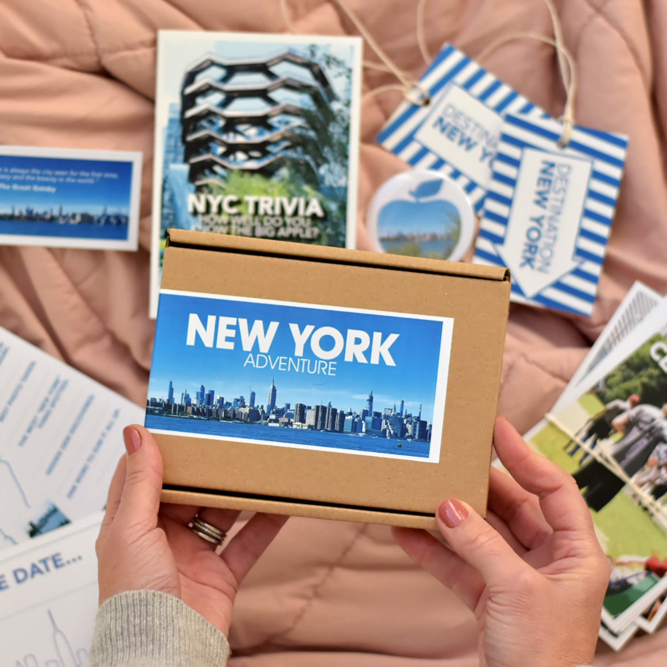 New York-themed travel kit with cards and a box held by hands on a soft surface.