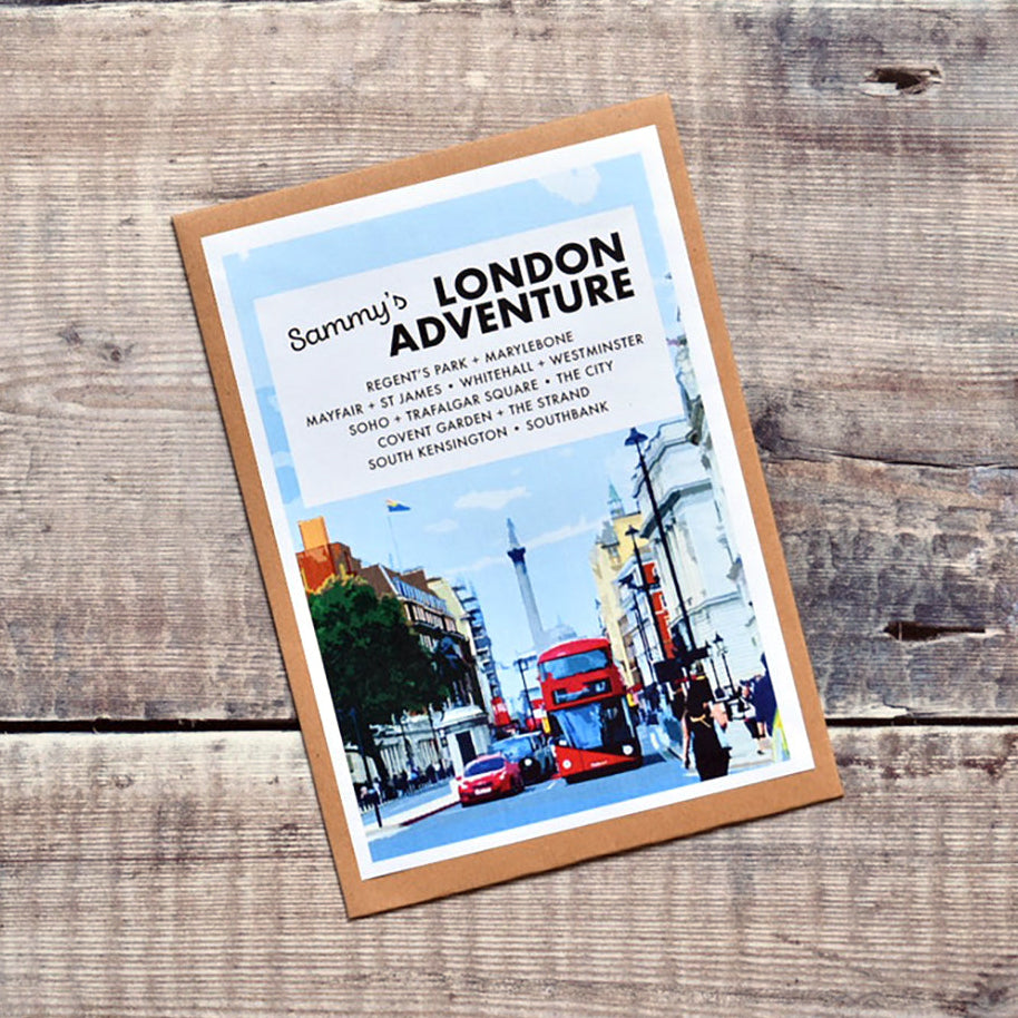 A personalised gift 'Sammi's London Adventure' displayed on a rustic wooden plank background. The cover of the London kit features a white top section with black text and a bottom section showing a colourful illustration of a classic red double-decker bus in London street traffic.