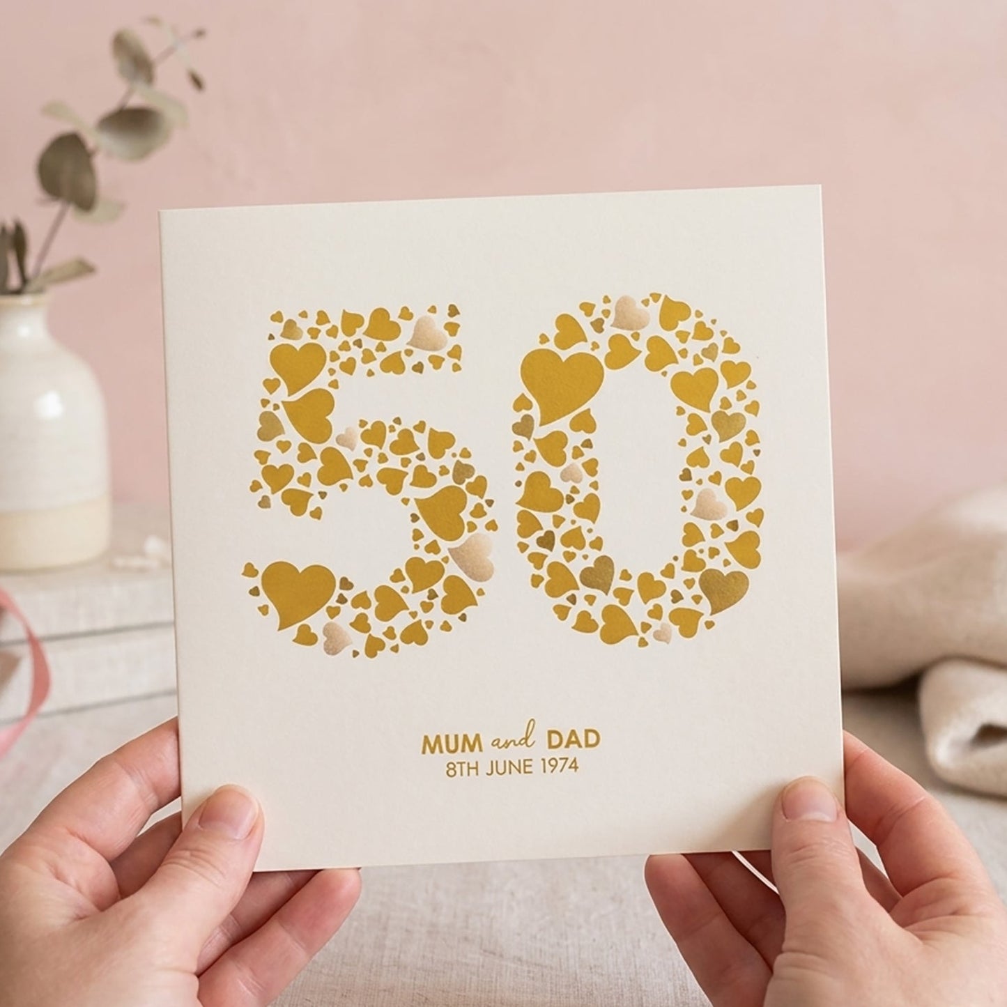Card with '50' design made from many love hearts in shades of gold. Underneath is personalised with the name of the couple and their wedding date.