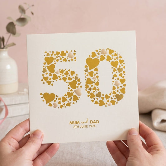 Card with '50' design made from many love hearts in shades of gold. Underneath is personalised with the name of the couple and their wedding date.
