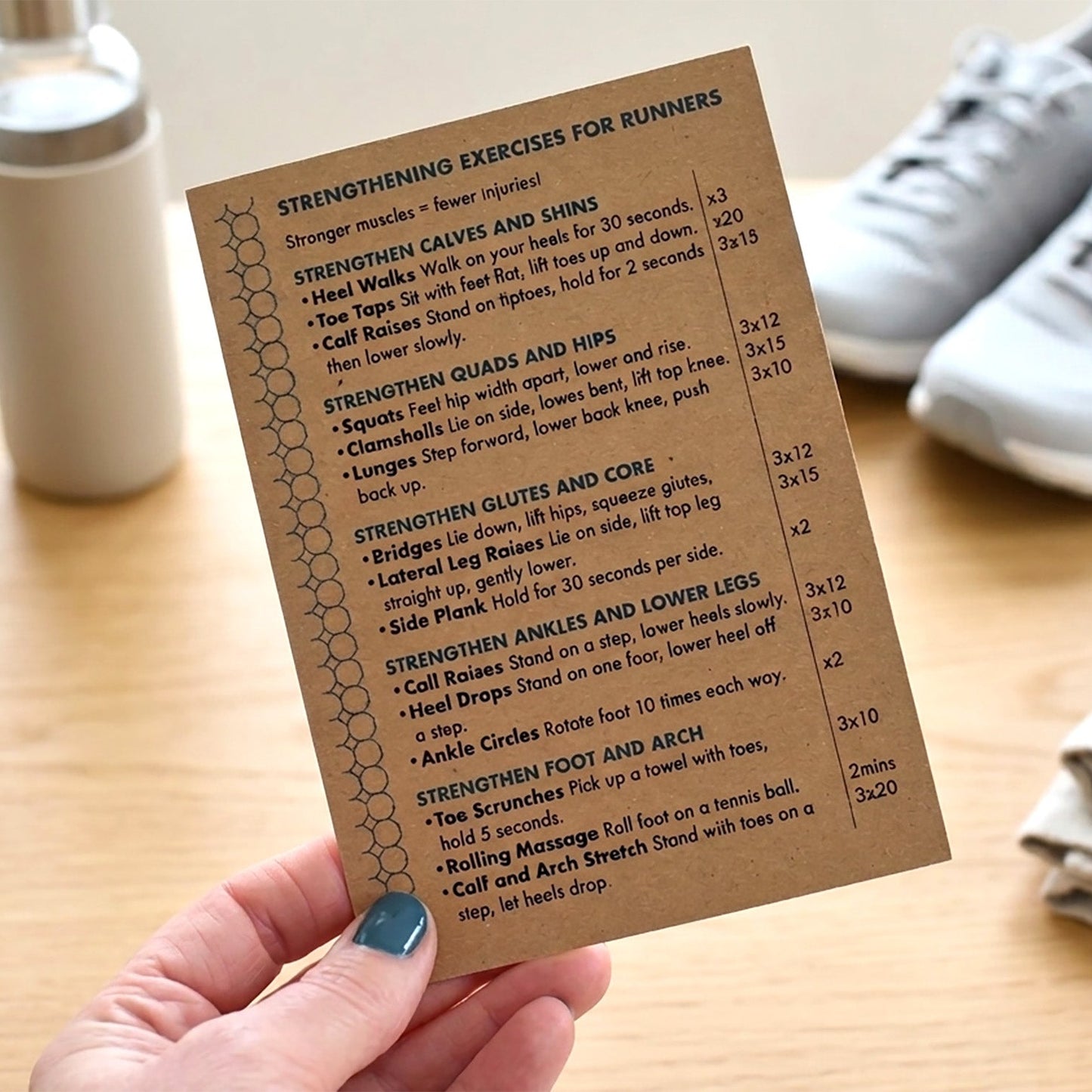 Hand holding a card with 'Strengthening Exercises for Runners' list on a wooden surface with trainers.