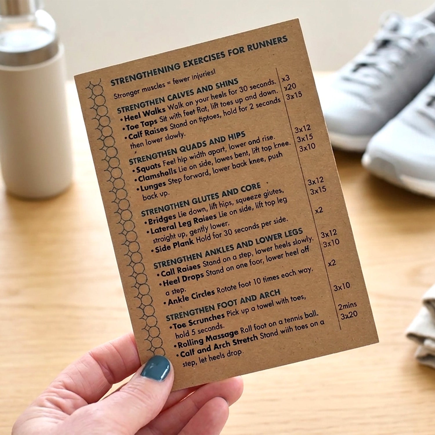 Hand holding a card with 'Strengthening Exercises for Runners' list on a wooden surface with trainers.