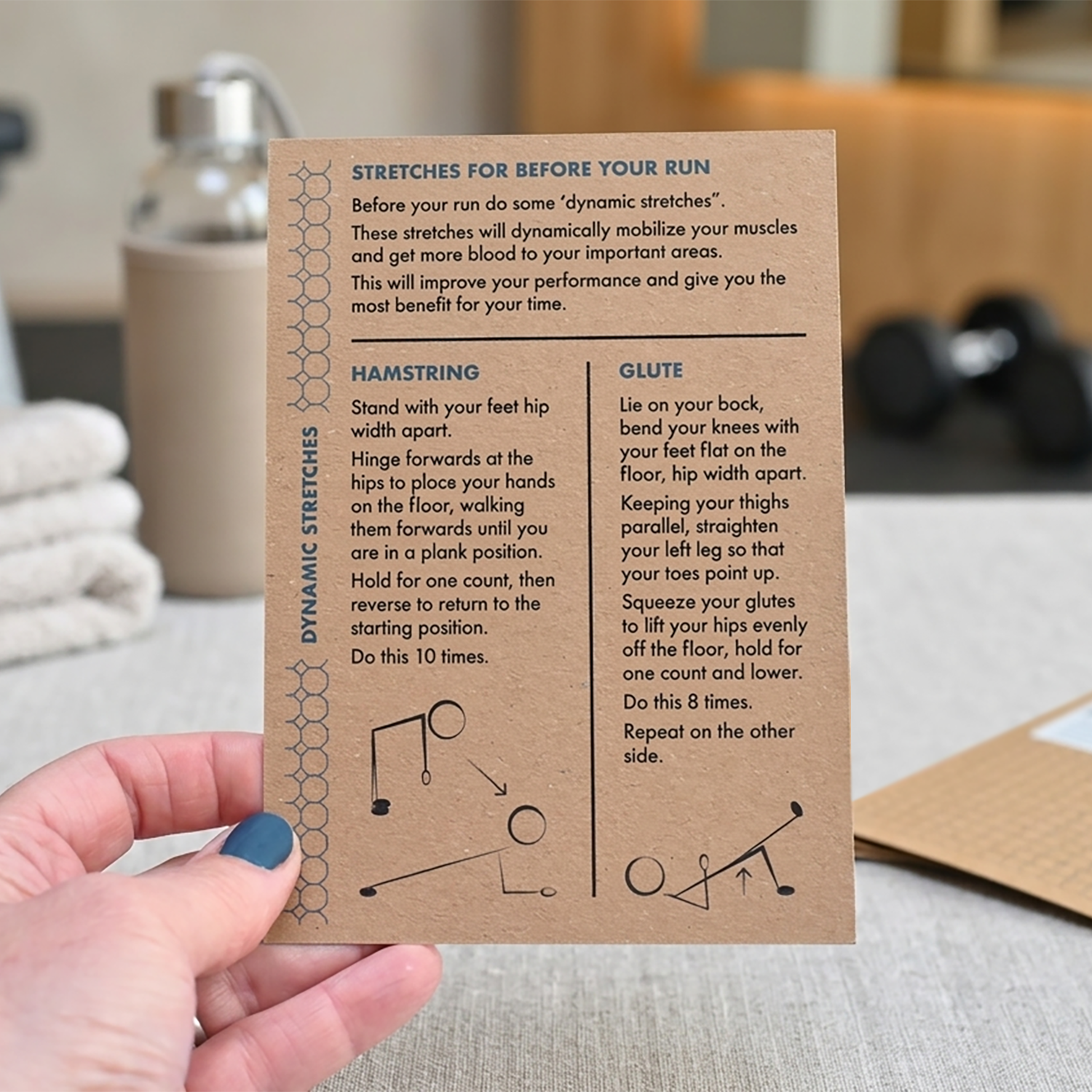 Hand holding a card with stretching exercises for before running, with a gym background.