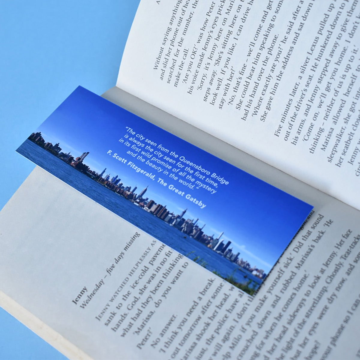 Hand holding a Bookmark with text and a  New York cityscape photo and a quote from The Great Gatsby.