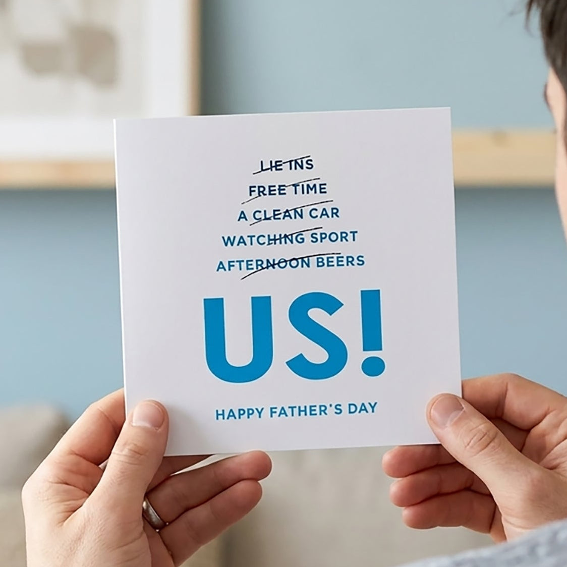Person holding a Father's Day card with text that reads Ombré blue text lists out all the things dad might hope for: "Lie-ins, Free Time, A Clean Car, Watching Sport, Afternoon Beers" — each one cheekily crossed out.

And in bold, unapologetic letters? “Us.”