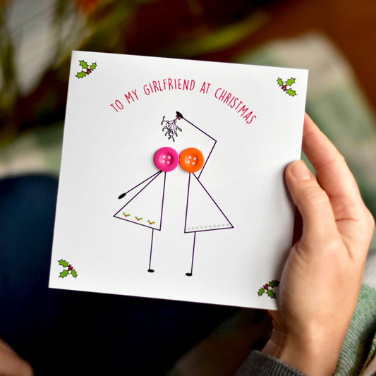To My Girlfriend at Christmas Card with 2 stick figure women with coloured buttons heads. The ladies are kissing under mistletoe.